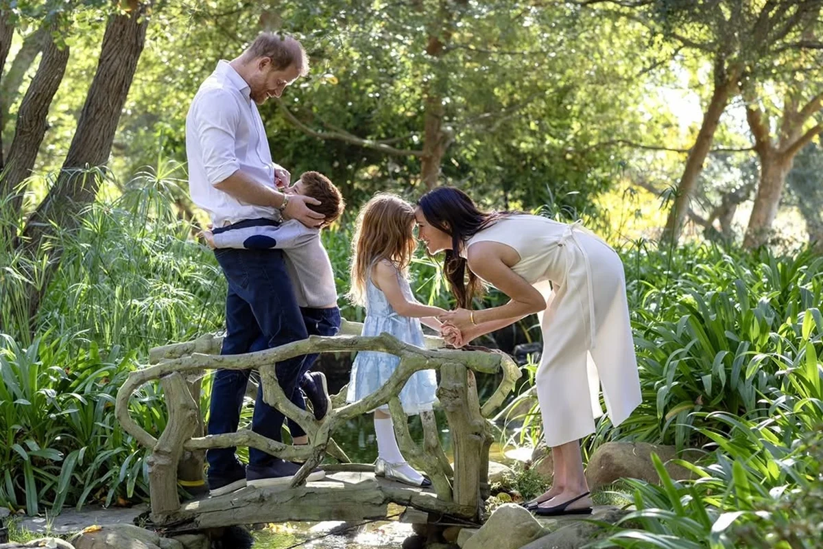 Foto colorida de homem, mulher e duas crianças em uma ponte e em um jardim, são Harry, Meghan e os filhos - Metrópoles
