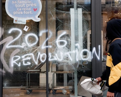 A passer-by looks at a cracked window with '2026 revolution' spray-painted onto it