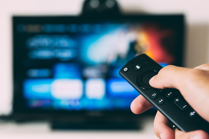 A hand holds a remote pointed towards a large TV.