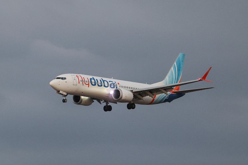A white, blue and orange flydubai Boeing 737 aircraft flies against an overcast sky